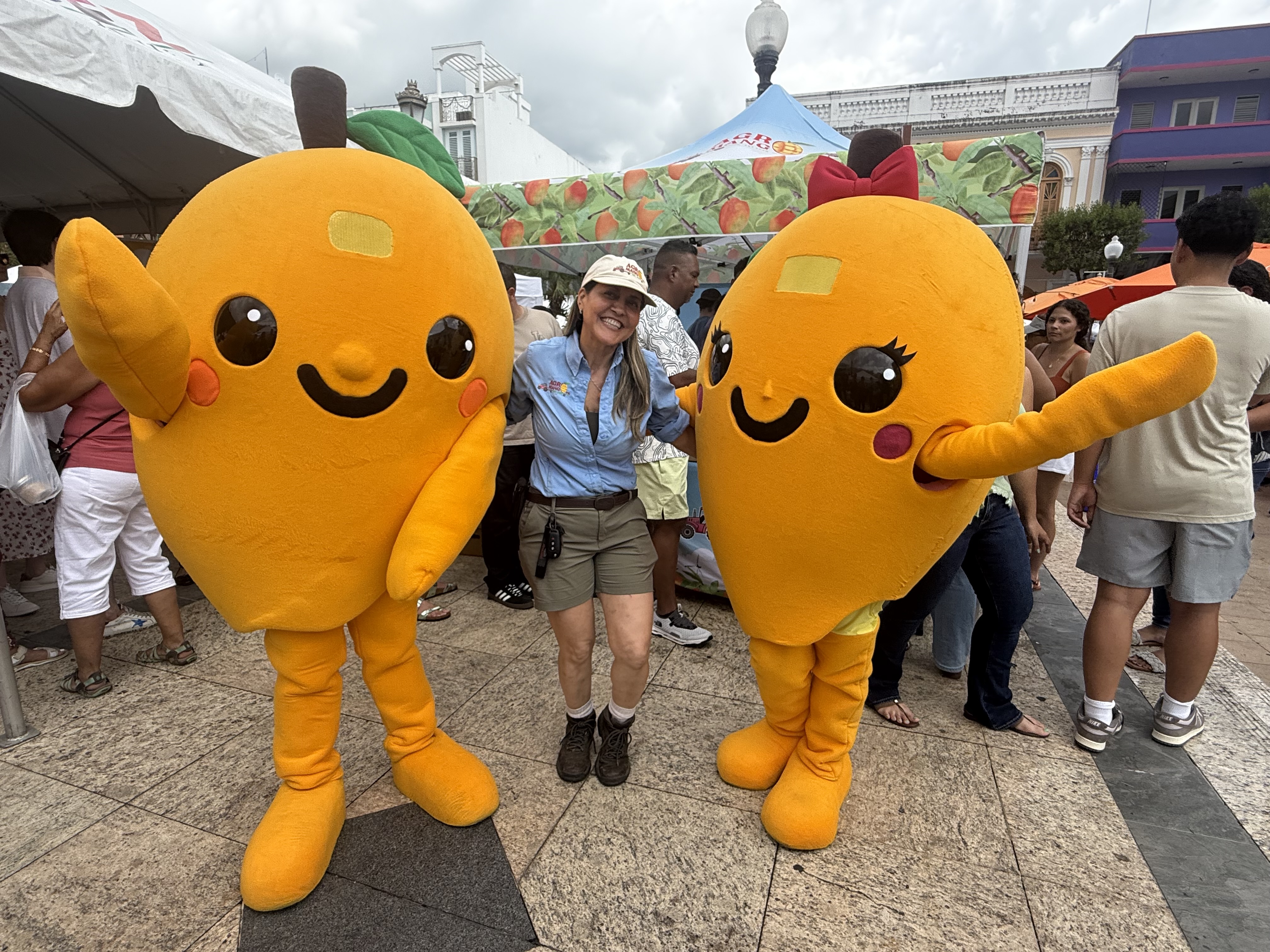 Mascotas del Festival del Mango con visitante en la Plaza Pública